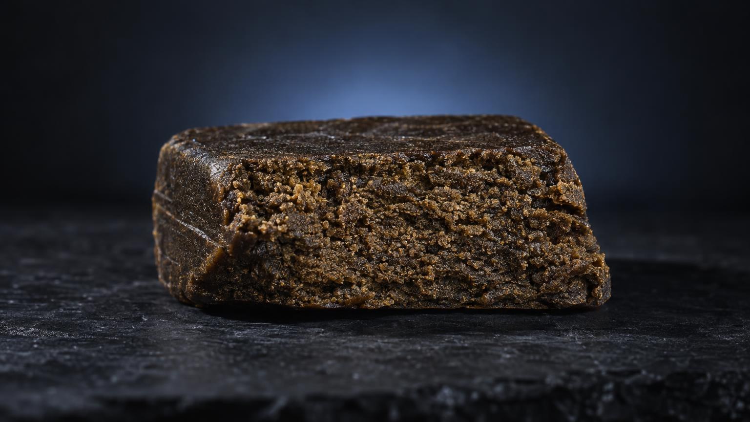 Bloc de hash aux teintes dorées et brunes sur surface sombre, montrant la texture granuleuse caractéristique du Curing hash