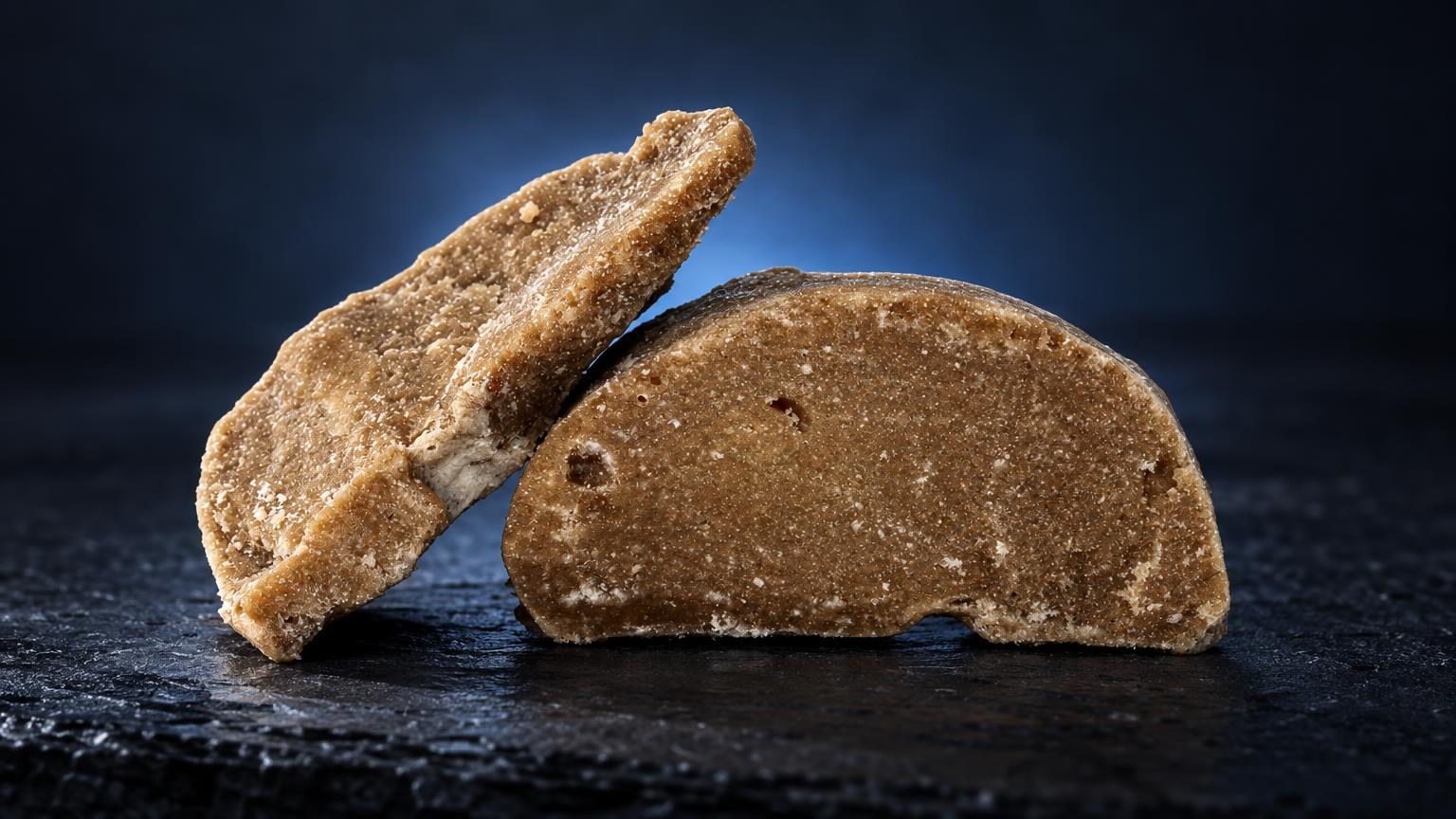 Deux morceaux de frozen hash de couleur dorée et beige, à texture granuleuse, posés sur surface noire