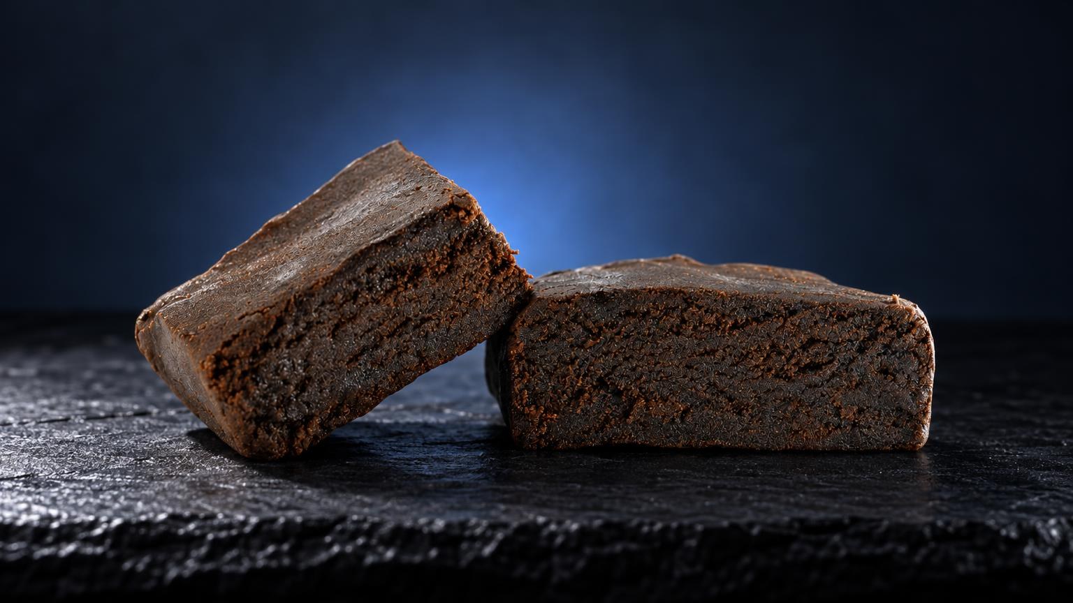 Two dense, brown hash blocks with crumbly texture on dark slate