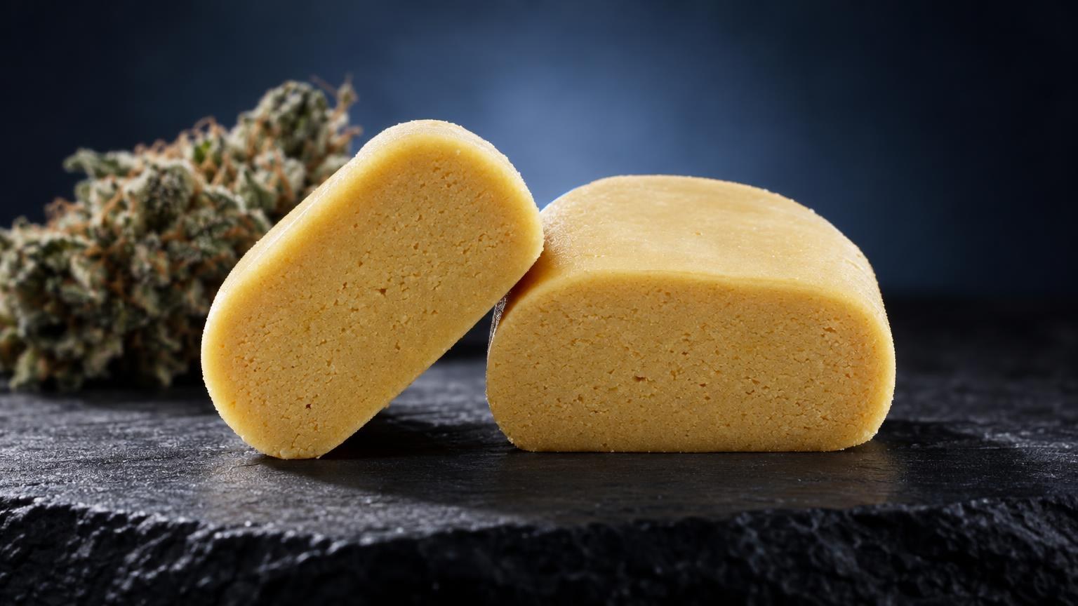 Piatella : deux plaques de hash dorées à texture granuleuse posées sur ardoise noire, avec fleur séchée en arrière-plan