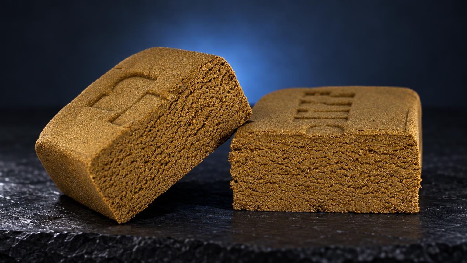 Deux blocs de Golden Hash de texture granuleuse dorée sur surface noire, concentré de Wax CBD aux formes géométriques